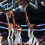 Dynamic college basketball game action shot with players competing for the ball under the basket during intense Big Ten conference matchup, arena lights illuminated, crowd energy visible