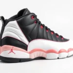 Professional product photography of black and white Air Jordan 12 sneaker with red accent stripes, displayed on neutral white background, studio lighting, photorealistic, side profile view, no text or logos visible