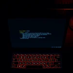 Atmospheric overhead shot of a laptop displaying glowing text on dark screen in dimly lit room, warm keyboard glow, immersive gaming environment