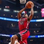 Professional NBA basketball player mid-jump shot during intense game action, arena lights blurred in background, sweat visible, dynamic motion captured