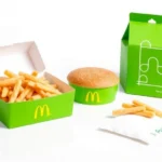 Vibrant green McDonald's packaging featuring Squid Game geometric symbols (circle, triangle, square) and minimalist design on a clean white surface, photorealistic product photography