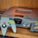Professional photo of vintage Nintendo 64 console with controller and cartridges displayed on wooden gaming shelf, warm ambient lighting highlighting metallic surfaces and classic gray hardware