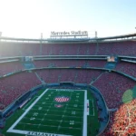 Overhead stadium view of Mercedes-Benz Stadium in Atlanta filled with thousands of enthusiastic college football fans wearing team colors, bright afternoon sunlight, championship atmosphere