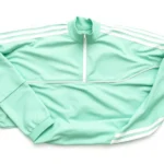 Close-up of vibrant mint-green tracksuit with white stripes laid flat on white background, showing fabric texture and stripe details photorealistically