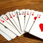 Close-up of playing cards fanned out on a wooden table, showing spades and hearts suits, natural lighting, professional card game setup
