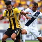 Professional football players in yellow Santos jersey and white Vasco da Gama jersey competing intensely for possession during daytime stadium match