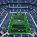 Aerial photograph of massive military stadium completely filled with thousands of uniformed cadets and sailors sitting in organized formations creating striking geometric patterns with distinct color sections, dramatic high angle view showcasing scale and tradition